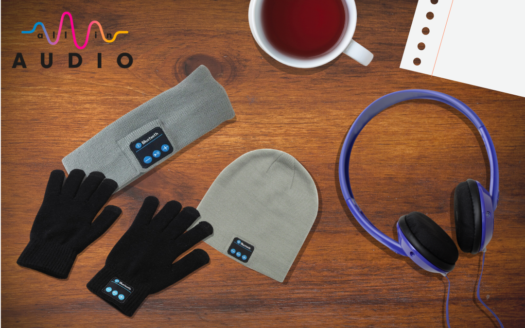Different types of audio apparel on a wooden desk. Wool hat, gloves, head band, and headphones.